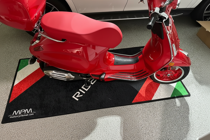 Vespa scooter on custom motorcycle pit mat in indoor garage, non-slip floor cover for stylish display setup.
