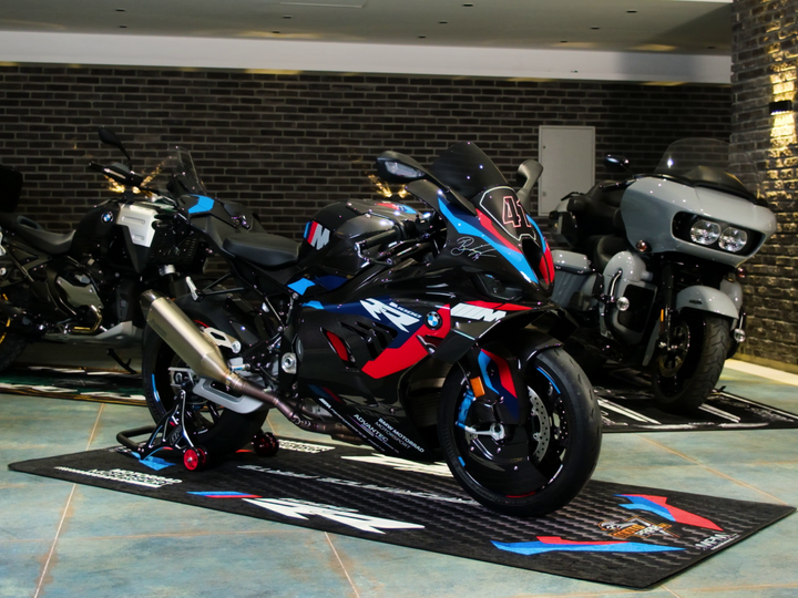 BMW M1000RR on custom motorcycle pit mat in premium indoor garage, non-slip floor cover for superbike display.